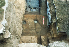 Vue du haut de l'enceinte, la tranchée fouillée au travers du fossé défensif du IIIe siècle. La partie effondrée du mur de l'amphithéâtre (brèche du VIIe siècle) se détache au premier plan, puis la lice (rive intérieure, côté ville), le fond du fossé et la rive sud.