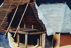 Proposition de restitution de deux maisons augustéennes de la phase -30 à +1. Les murs sont réalisés en briques de terre crue (adobe), protégée intérieurement et extérieurement par un enduit à la chaux de couleur bleue, noire ou ocre. À l'extérieur ont été observés des creusements et des calages correspondant à l'implantation de poteaux d'angle. À l'intérieur, le sol en terre battue est bordé de tranchées de drainage remplies de graviers. Des poteaux implantés à l'intérieur constituaient la structure porteuse de la toiture, dissociée des murs écrans en terre. Maquette J. Parreaux et G. Mauguin, Besançon.
