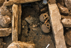 Tombe &agrave; cr&eacute;mation en coffrage de dalles, d&eacute;but IIe si&egrave;cle apr&egrave;s J.-C.  Le d&eacute;p&ocirc;t a &eacute;t&eacute; install&eacute; dans la fosse utilis&eacute;e pour br&ucirc;ler le corps. Il comprend des vases &eacute;voquant les libations effectu&eacute;es en honneur du d&eacute;funt&nbsp;: deux cruches en c&eacute;ramique et deux r&eacute;cipients en verre, un balsamaire et un gobelet plac&eacute; &agrave; l'envers, en un geste rituel destin&eacute; &agrave; marquer la s&eacute;paration entre le mort et les vivants.  78 avenue Jean-Jaur&egrave;s, N&icirc;mes (Gard), 2003.  &copy; Brigitte Thuillier, Inrap