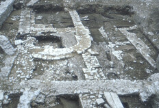 Une lecture difficile des constructions monumentales, Haut Empire  La surface d&eacute;cap&eacute;e vue depuis l'est montre un effet de palimpseste avec la succession des phases d'occupation. Les solins de pierres &eacute;troits des maisons tardo-r&eacute;publicaines, visibles &agrave; droite du clich&eacute;, sont recoup&eacute;s par les fondations plus puissantes des &eacute;difices monumentaux du centre public antique -blocs de pierre taille au premier plan et grande excavation de la fondation du podium. L'ensemble est impact&eacute; par les fondations de l'&eacute;glise m&eacute;di&eacute;vale et les murs au mortier gris du th&eacute;&acirc;tre contemporain.  N&icirc;mes, Ancien th&eacute;&acirc;tre (Gard), 1985.  &copy; Francis Cognard, Fonds Arch&eacute;Ofactory