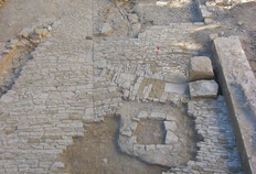 La cour &eacute;troite entre trois b&acirc;timents des XIIIe et XIVe si&egrave;cles avec son pavement refait au XVe si&egrave;cle.  On note la partie souterraine carr&eacute;e du puits au premier plan et les fils d'eau au milieu du pavage qui dirigent les eaux de pluie vers la citerne et des drains souterrains.  Place du Chapitre, N&icirc;mes (Gard), 2005  &copy; Richard Pell&eacute;, Inrap
