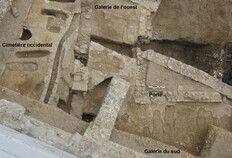 Angle sud-ouest du campo santo au XIVe si&egrave;cle, vu du sud.  &Agrave; gauche, sur l'espace du cimeti&egrave;re occidental, vestiges du sol de terre orang&eacute;, des tombes et la canalisation empierr&eacute;e d'un &eacute;tat post&eacute;rieur. &Agrave; droite, les galeries de l'ouest et du sud avec leurs tombes en fosse (non fouill&eacute;es) se d&eacute;coupant sur le vestige de la chape blanche chaul&eacute;e qui supportait un dallage de pierres. Celui-ci a &eacute;t&eacute; r&eacute;cup&eacute;r&eacute; lors de la d&eacute;molition du site.  Zac du Forum des Carmes � 5, N&icirc;mes (Gard), 2011  &copy; Benjamin Thomas, Inrap