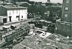 Vue g&eacute;n&eacute;rale de la fouille avec l'avenue Jean-Jaur&egrave;s en arri&egrave;re-plan.  Le clich&eacute; montre les conditions difficiles dans lesquelles s'est effectu&eacute;e la fouille, alors qu'une partie du terrain &eacute;tait d&eacute;j&agrave; en cours de construction.  &Eacute;cole Jean-Jaur&egrave;s, 14-16 avenue Jean-Jaur&egrave;s, N&icirc;mes (Gard), 1981  &copy; Pierre-Yves Genty, DRAC Languedoc-Roussillon, Service r&eacute;gional de l'Arch&eacute;ologie