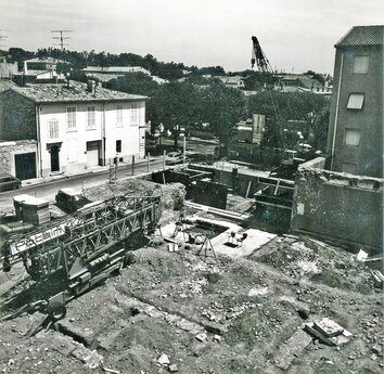 Vue g&eacute;n&eacute;rale de la fouille avec l'avenue Jean-Jaur&egrave;s en arri&egrave;re-plan.  Le clich&eacute; montre les conditions difficiles dans lesquelles s'est effectu&eacute;e la fouille, alors qu'une partie du terrain &eacute;tait d&eacute;j&agrave; en cours de construction.  &Eacute;cole Jean-Jaur&egrave;s, 14-16 avenue Jean-Jaur&egrave;s, N&icirc;mes (Gard), 1981  &copy; Pierre-Yves Genty, DRAC Languedoc-Roussillon, Service r&eacute;gional de l'Arch&eacute;ologie 